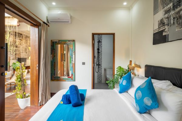 Luxurious Balinese bedroom with king bed, blue accents, open doors to lush garden, and en-suite shower.