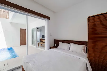 Modern bedroom with a king-sized white bed, wooden accents, and sliding glass doors opening to a private outdoor pool.