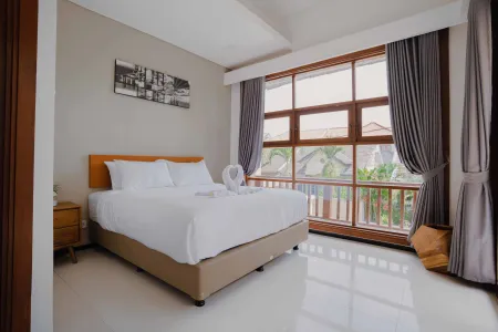 Modern bedroom with white-sheeted bed, wooden accents, large window to tropical garden, and abstract wall art.