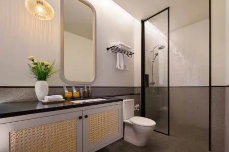 Modern minimalist bathroom featuring a black countertop vanity, oval mirror, glass shower enclosure, white toilet, and vase of yellow flowers. - Bali Villas