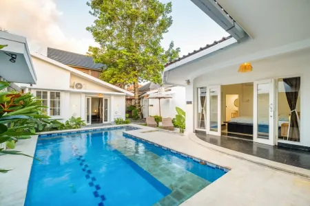 Serene Bali villa infinity pool surrounded by white architecture, lush tropical plants, and open bedroom suites at dusk.