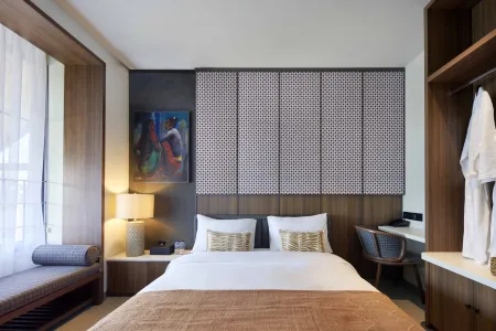 Modern luxury hotel bedroom with king bed, wooden accents, abstract wall art, desk, and window bench.