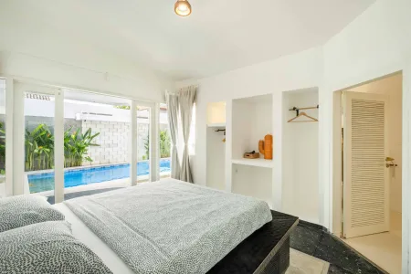Modern white bedroom with king bed, floor-to-ceiling windows overlooking infinity pool and tropical plants.