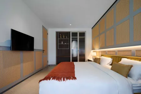 Modern bedroom interior with king-size bed, orange throw blanket, wall-mounted TV, and bamboo-accented walls.