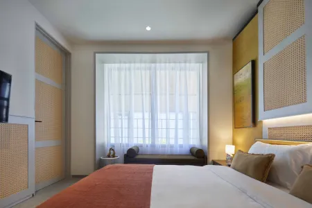 Modern bedroom with rattan wall panels, large curtained window, orange bed linens, and a plush daybed.