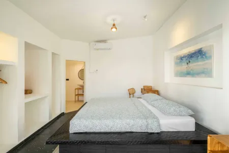 Modern minimalist bedroom with low platform bed, white walls, wooden accents, and abstract blue seascape painting.