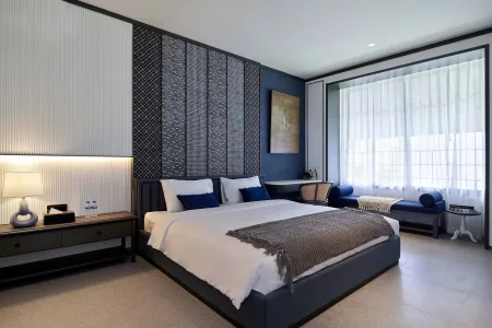 Modern luxury bedroom with navy bed, textured walls, sheer-curtained window, and blue chaise lounge.