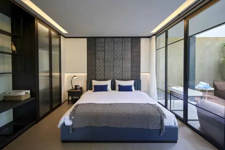 Modern minimalist bedroom with king-size bed, textured headboard, built-in wardrobes, and sliding glass doors to lush outdoor patio.