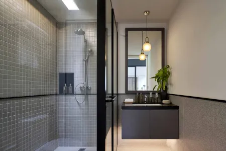 Modern minimalist bathroom with gray tiled walk-in shower, sleek black-framed vanity, pendant-lit round mirror, and potted plant. - Bali Villas