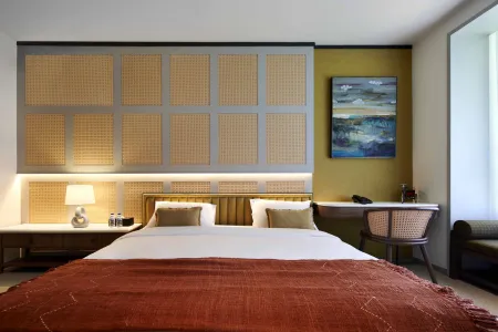 Modern luxury bedroom featuring a king bed with terracotta woven throw, rattan headboard, abstract blue painting, and wicker desk.