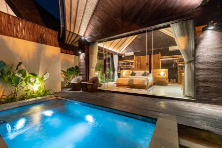 Luxurious tropical villa bedroom with private plunge pool and sliding glass doors, illuminated at night.