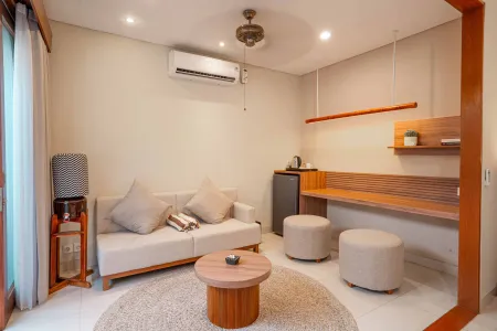 Cozy minimalist hotel suite living area with beige sofa, wooden coffee table, poufs, and tropical wood accents. - Bali Villas