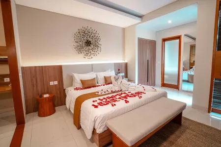 Luxurious Balinese bedroom suite with king bed adorned in red rose petals, towel swan, and champagne bottle.
