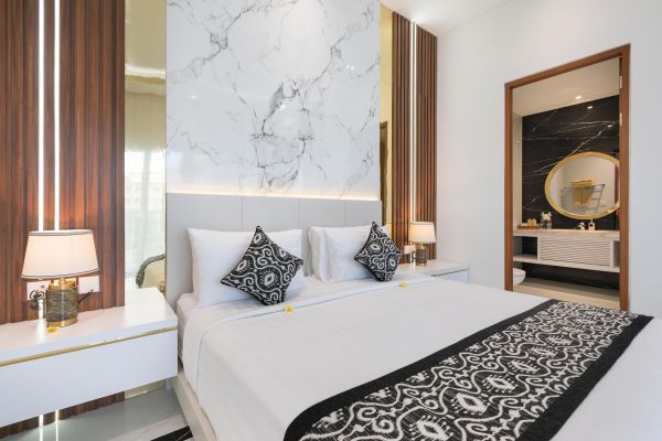 Luxurious modern bedroom with king-sized white bed, black patterned accents, marble walls, gold lamps, and open door to en-suite bathroom.