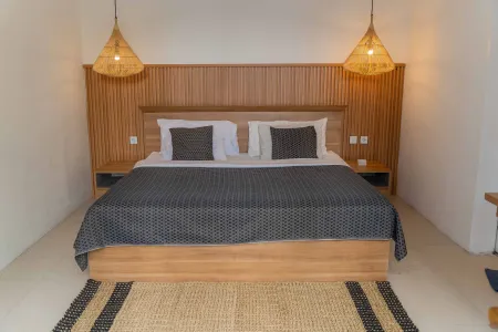 Modern wooden bed with gray bedding in minimalist white-walled bedroom, rattan pendant lights, and woven rug. - Bali Villas