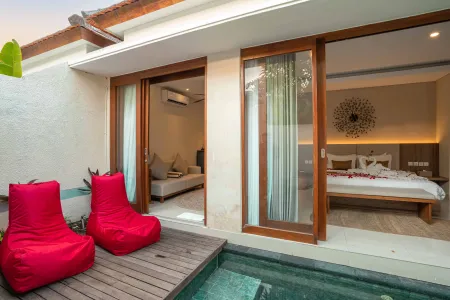Luxurious Bali pool villa with private plunge pool, red bean bag chairs, and open doors to a rose petal-adorned bedroom. - Bali Villas