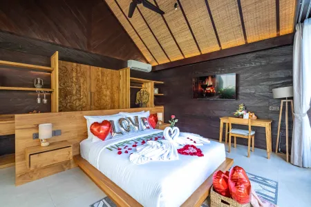 Romantic Balinese villa bedroom with heart-shaped balloons, rose petal-strewn bed, towel swans, and "LOVE" pillows for a honeymoon vibe.