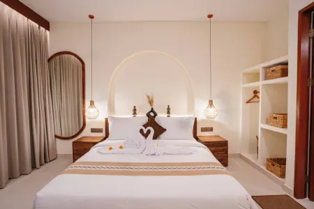 Cozy Balinese bedroom with king bed adorned in white linens and towel swans, arched niche headboard, pendant lights, round mirror, and woven basket shelves.