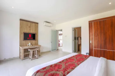 Spacious Balinese-style luxury bedroom with king bed, wooden desk, wall-mounted TV, and en-suite bathroom.