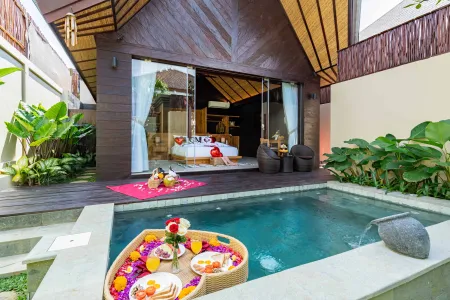 Romantic Balinese villa bedroom with private plunge pool and heart-shaped floating breakfast tray of flowers, fruits, and pastries.