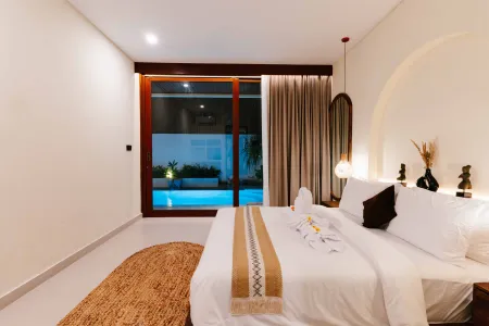 Luxurious tropical bedroom with king bed and private infinity pool view through glass doors at night.