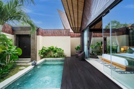 Luxurious Balinese-style villa with private turquoise pool, wooden deck, sliding glass doors to bedroom, and tropical palm surroundings.