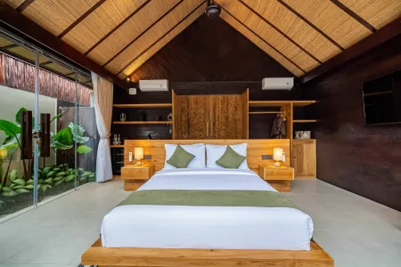 Spacious Balinese-style bedroom with wooden king bed, tropical plants, and garden view through glass doors.