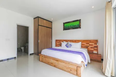 Spacious modern bedroom with wooden platform bed, purple accents, tropical green painting, and en-suite bathroom in a Bali villa.