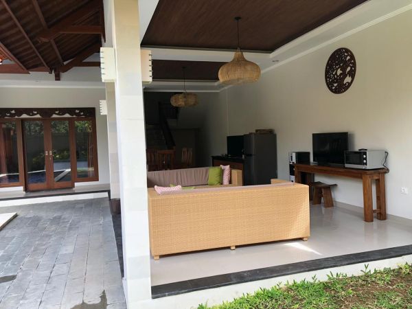 Spacious Balinese villa living room with rattan sofa, wooden accents, TV setup, and open view to tropical garden. - Bali Villas