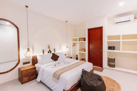 Cozy Balinese-style bedroom with wooden bed, white linens adorned with frangipani, pendant lights, woven rug, and tropical decor.