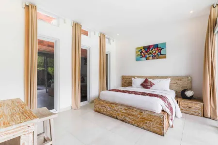 Bright tropical bedroom with wooden bed, colorful abstract art, beige curtains, and garden view.