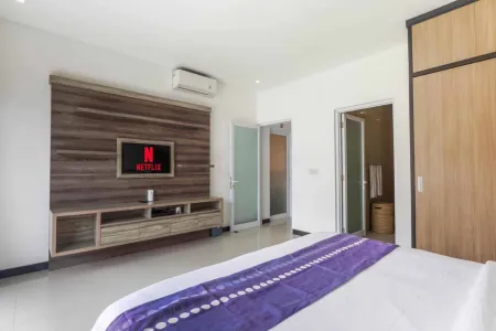 Modern hotel bedroom with wooden wall-mounted TV showing Netflix, king bed with purple runner, and built-in oak cabinetry.