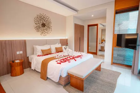Romantic Balinese villa bedroom with king bed adorned in red rose petals, towel swan, wooden accents, and open bathroom view.