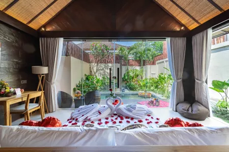 Romantic Balinese villa bedroom with swan towel art, rose petals on white linens, and open doors to lush garden pool.