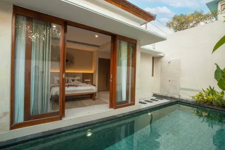 Luxurious Balinese villa bedroom with open wooden sliding doors leading to a private infinity pool, surrounded by tropical greenery.