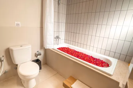 Luxurious bathroom with a white bathtub filled with vibrant red rose petals, flanked by a toilet and tiled shower area. - Bali Villas
