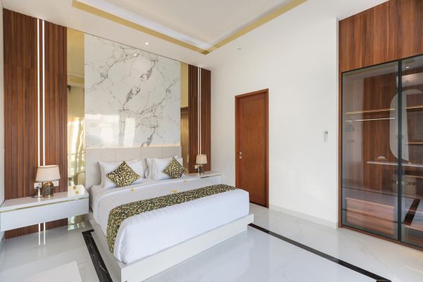Elegant modern bedroom featuring a white king-sized bed with green patterned bedding, marble feature wall, wooden wardrobe, and soft lighting in a luxury villa. - Bali Villas