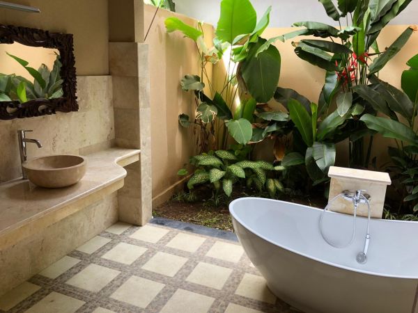 Serene tropical bathroom with stone sink, freestanding white bathtub, and lush green plants. - Bali Villas