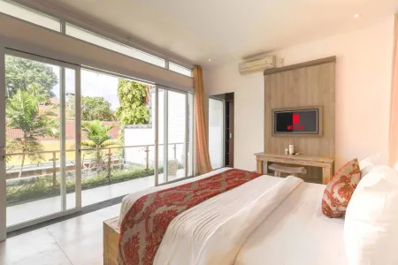 Spacious tropical bedroom with king bed in red floral bedding, sliding glass doors to lush garden view, and wall-mounted TV.