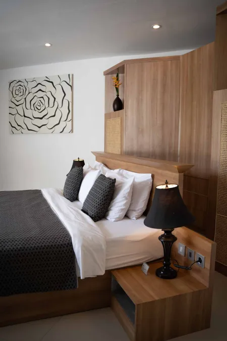 Cozy tropical bedroom with wooden king bed, gray duvet, black lamps, rose wall art, and rattan wardrobe.