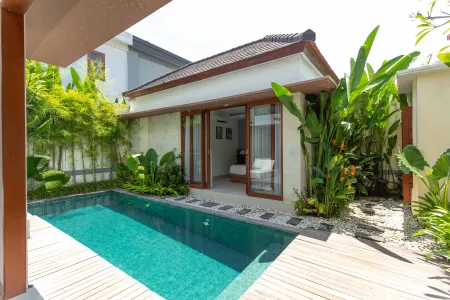 Tropical Bali villa with infinity-edge pool, lush greenery, and open sliding doors to a serene bedroom.
