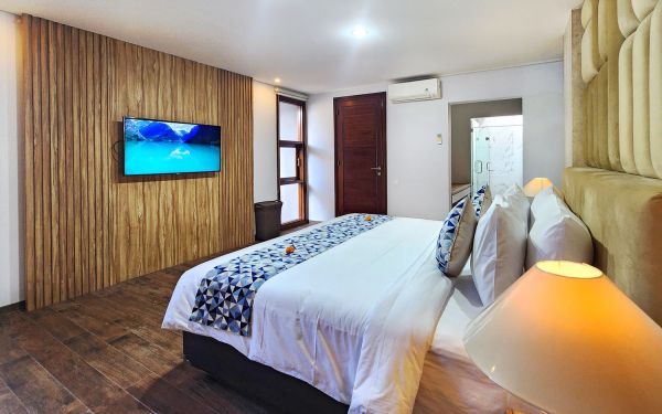 Spacious Bali villa bedroom with wooden paneled walls, king bed in blue and white linens, wall-mounted TV, and balcony access.