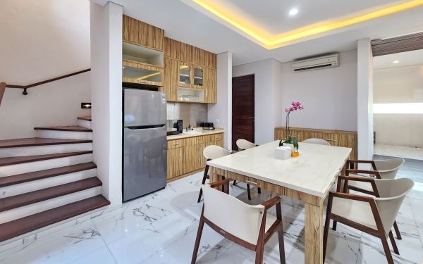 Modern open-plan kitchen and dining area with wooden cabinets, marble-top table, stainless steel fridge, and potted orchids in a Balinese villa. - Bali Villas