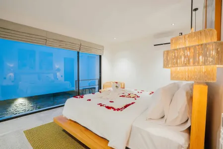 Romantic luxury bedroom with heart-shaped rose petals on a white bed, featuring a large ocean-view window at dusk.