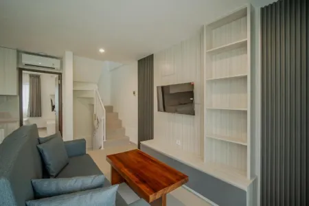 Modern minimalist living room interior with gray sofa, wooden coffee table, wall-mounted TV, built-in white shelves, and adjacent stairs. - Bali Villas