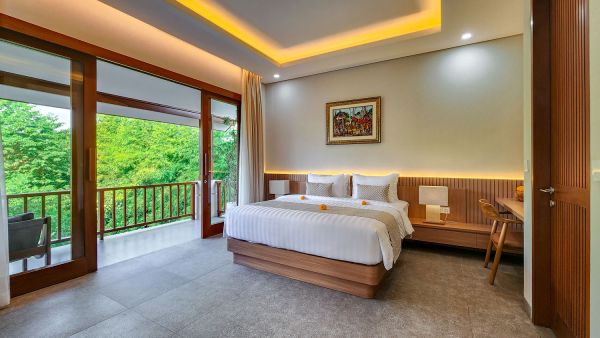 Luxurious tropical bedroom with wooden king bed, sliding doors to lush green balcony, and Balinese artwork in a modern villa.