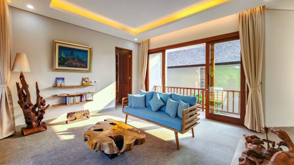 Cozy Balinese villa living room with blue sofa, wooden root coffee table, carved statues, and open doors to lush balcony. - Bali Villas