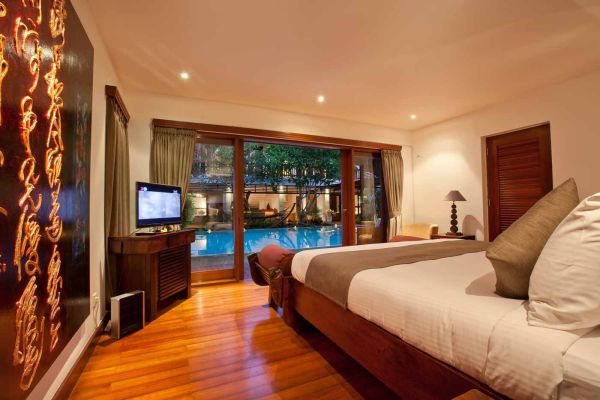 Luxurious tropical bedroom with king bed, wooden accents, and sliding doors to private pool view.
