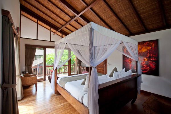 Elegant Balinese bedroom with white-canopy four-poster bed, tropical balcony view, and wooden accents. - Bali Villas