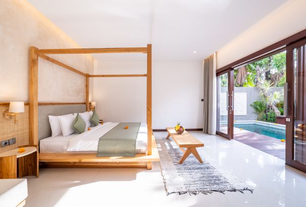 Serene Balinese bedroom with wooden four-poster bed, green bedding, and sliding doors to lush garden infinity pool. - Bali Villas